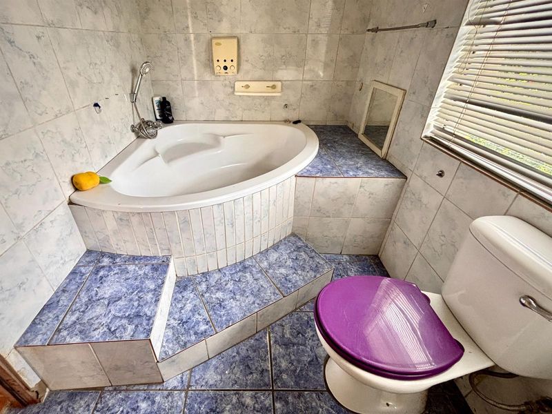 A dated bathroom featuring a corner bathtub with tiled surround, floor-to-ceiling wall tiles, and a standard toilet.