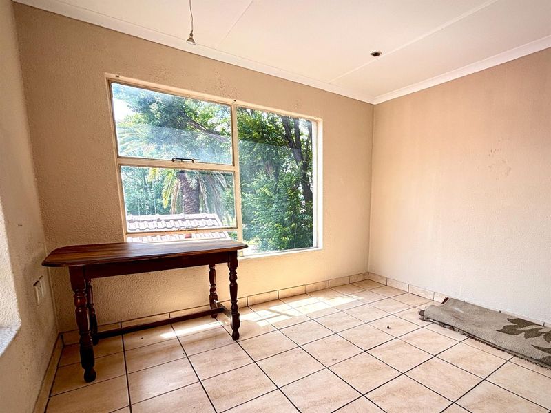 A bright, empty room featuring neutral tiled flooring and a large window providing natural light and garden views.