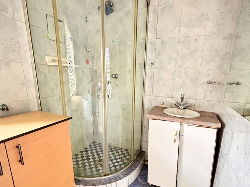 A dated bathroom featuring a corner shower enclosure, a small vanity unit with a basin, and blue floor tiling.