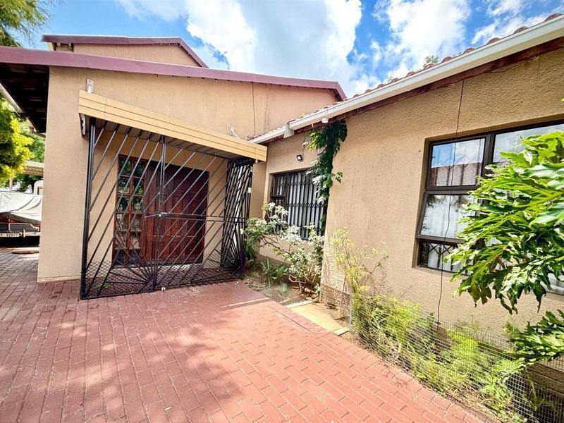 Exterior view of the property entrance featuring a paved driveway, security gate, and established garden beds against the building facade.