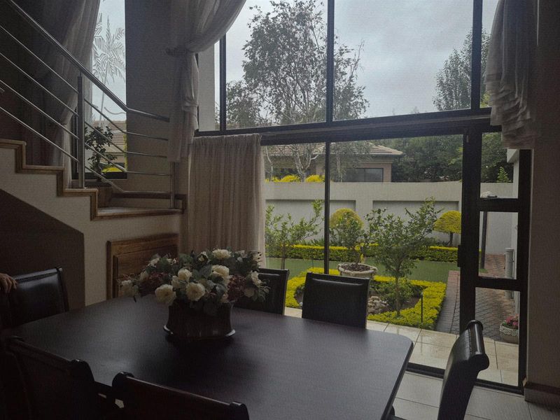 Dining area featuring floor-to-ceiling windows with garden views, tiled flooring, and a modern staircase with stainless steel railings.