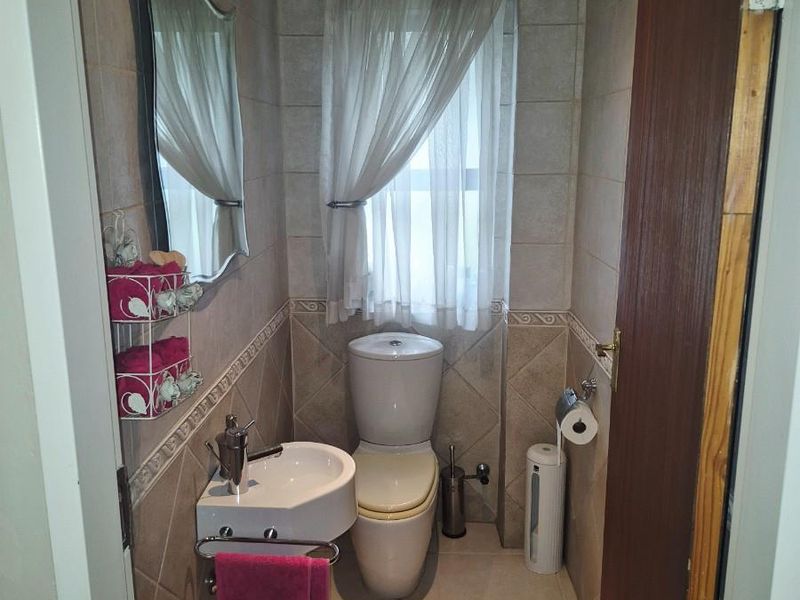 A compact guest bathroom featuring neutral ceramic wall and floor tiles, a wall-mounted basin, and a standard toilet.