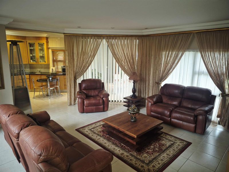 Open plan living area featuring tiled floors and an integrated kitchen with wooden cabinetry, flowing into a spacious lounge area with large windows.