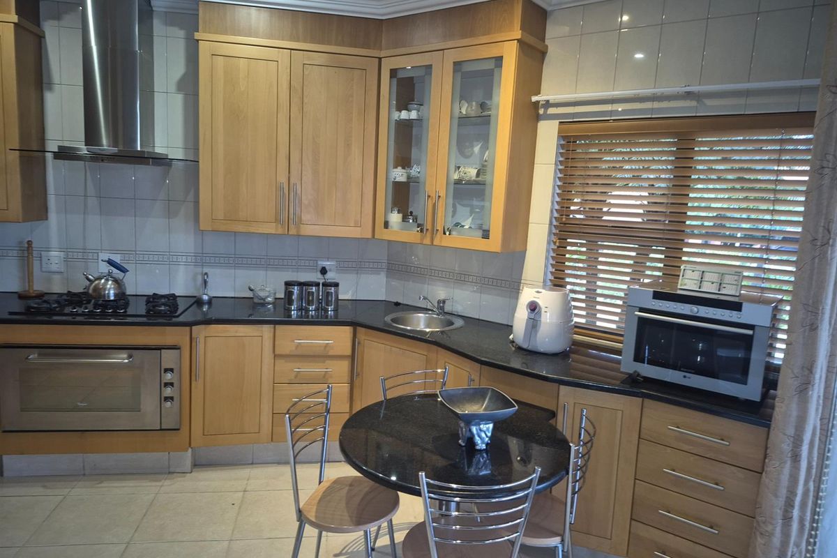 A functional kitchen featuring light wood cabinetry, granite countertops, a gas hob, built-in oven, and a dedicated breakfast nook area.