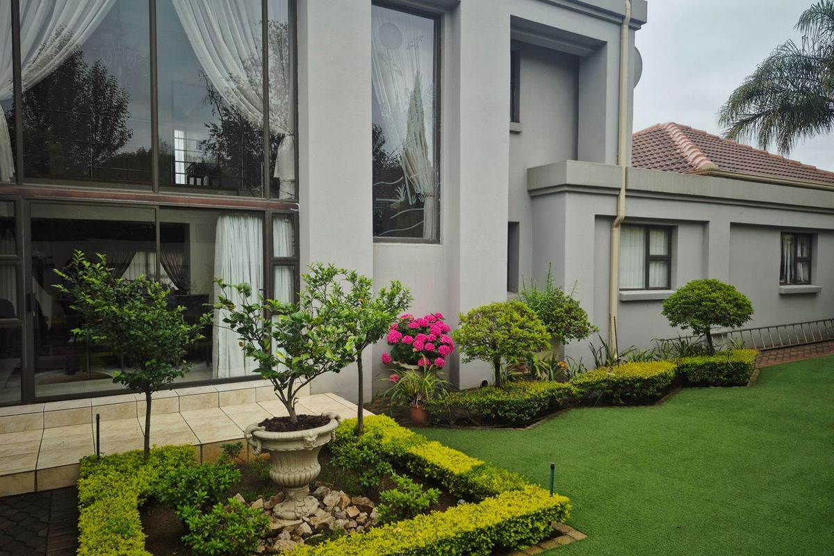Rear view of a modern double-storey house featuring large glass sliding doors, a tiled patio area, and a well-maintained landscaped garden with artificial lawn.