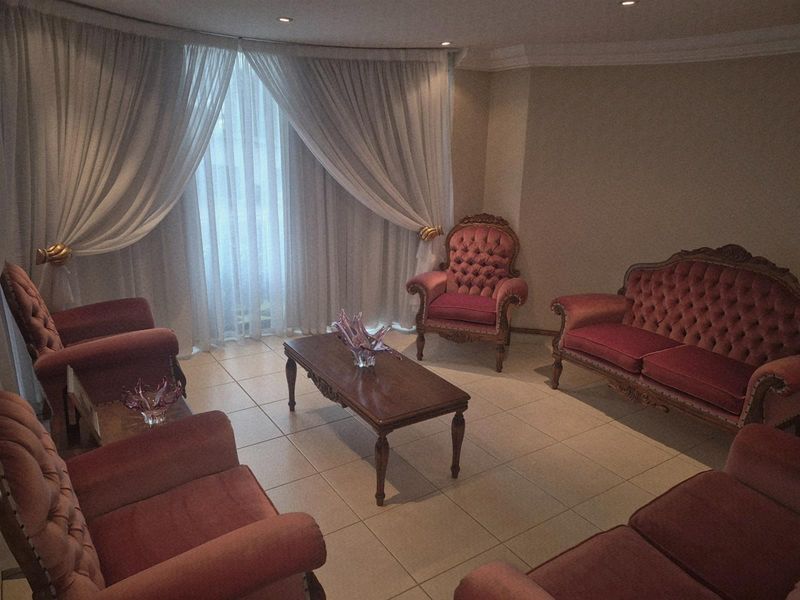 A formal living room featuring tiled flooring, recessed downlights, and large windows dressed with floor-to-ceiling curtains.