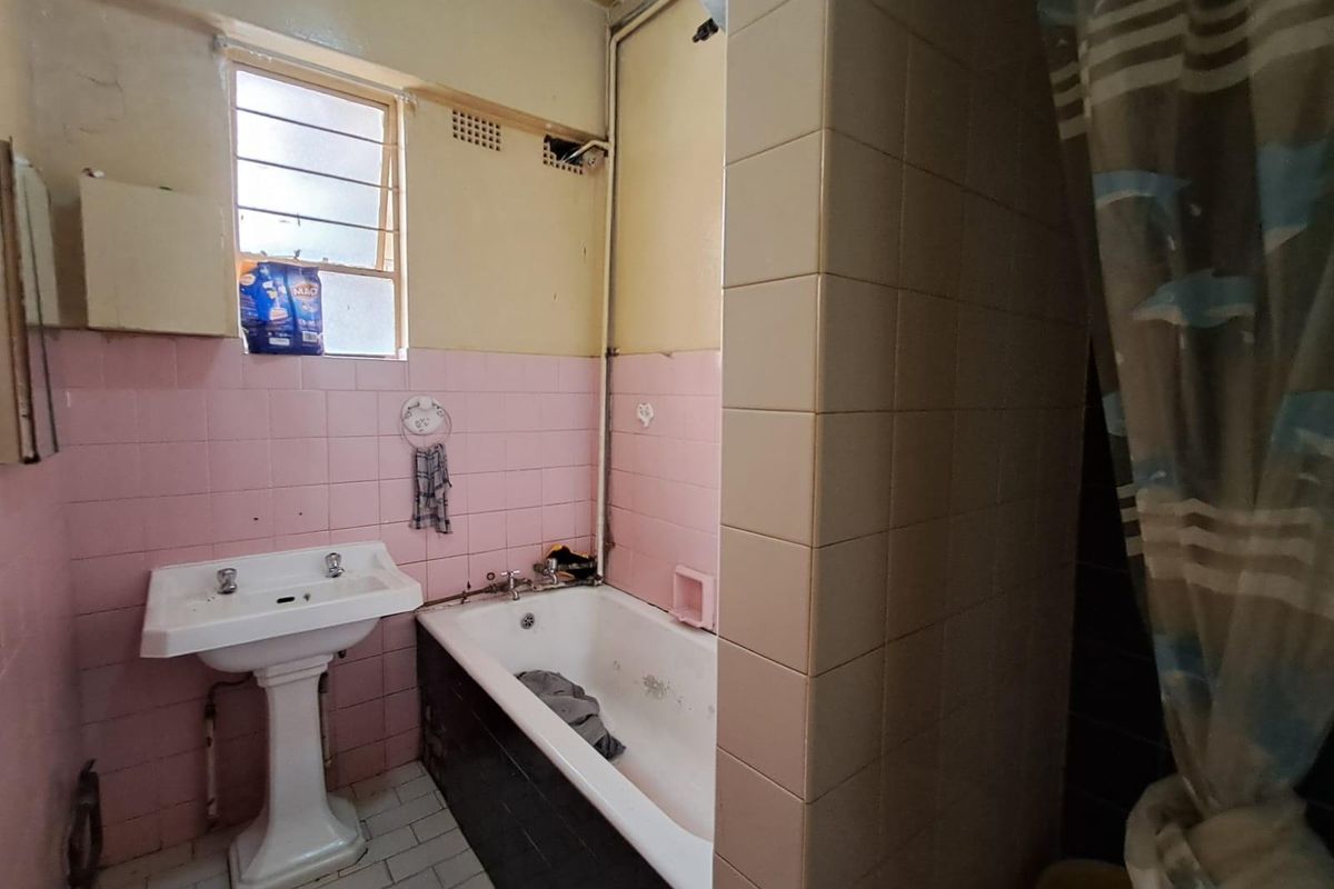 A dated bathroom featuring a pedestal sink, a bathtub with shower curtain, and original pink wall tiling requiring renovation.