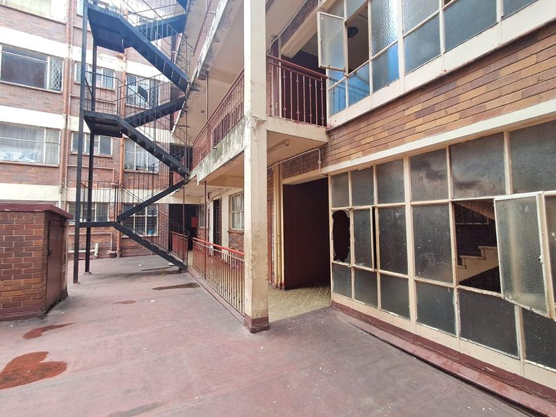 Exterior view of an apartment building featuring a metal fire escape staircase, brick facade, and multiple windows with visible signs of wear and damage.