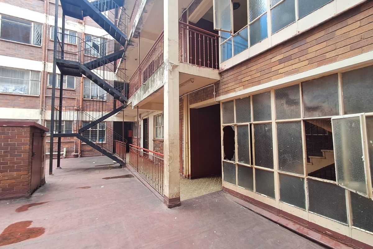Exterior view of an apartment building featuring a metal fire escape staircase, brick facade, and multiple windows with visible signs of wear and damage.