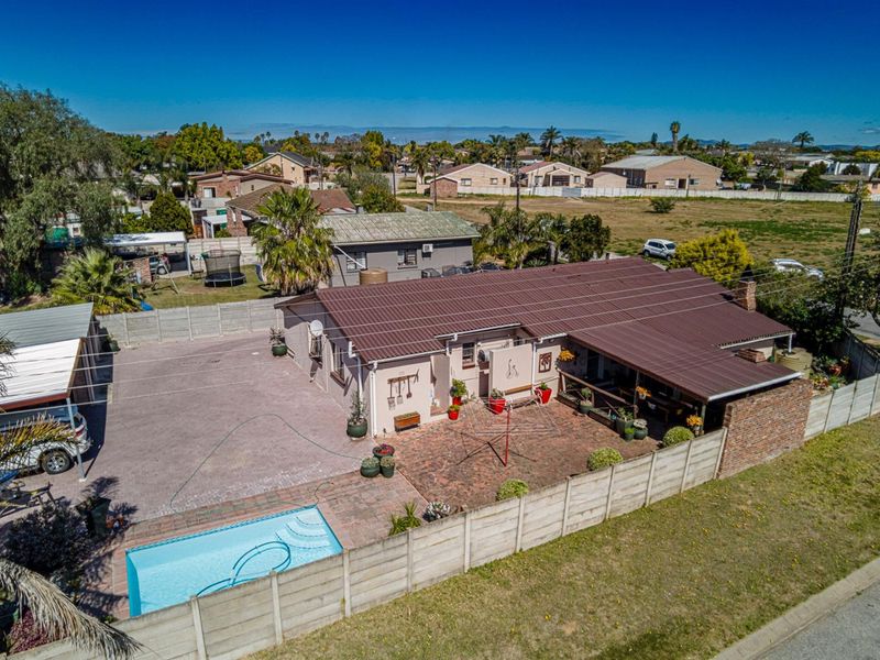 Aerial view of a residential property featuring a swimming pool, paved patio area, metal roofing, and secure boundary walling.