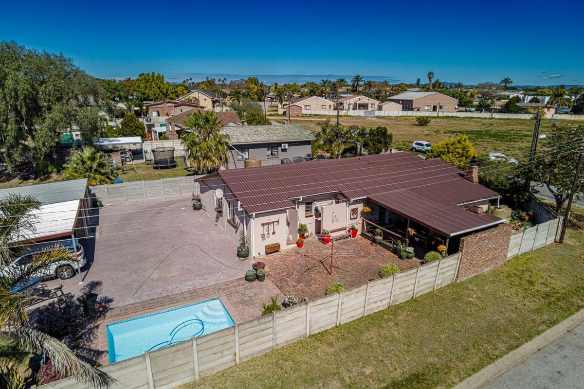 Aerial view of a residential property featuring a swimming pool, paved patio area, metal roofing, and secure boundary walling.