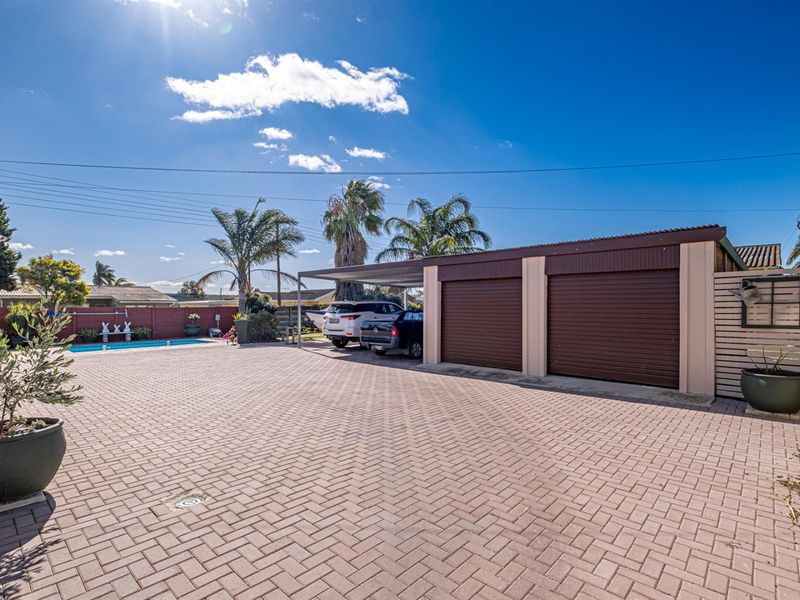 Spacious paved rear yard featuring a double garage, attached carport, and a swimming pool, providing ample parking and outdoor entertainment space.
