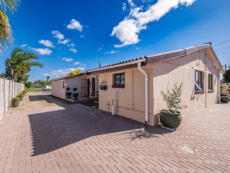 A view of the rear exterior of the house featuring a paved driveway, boundary wall, and functional guttering system.