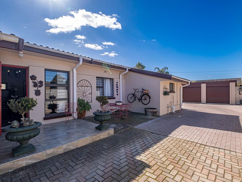 Rear exterior view featuring a paved driveway, tiled patio area, and access to a double garage with roller doors.
