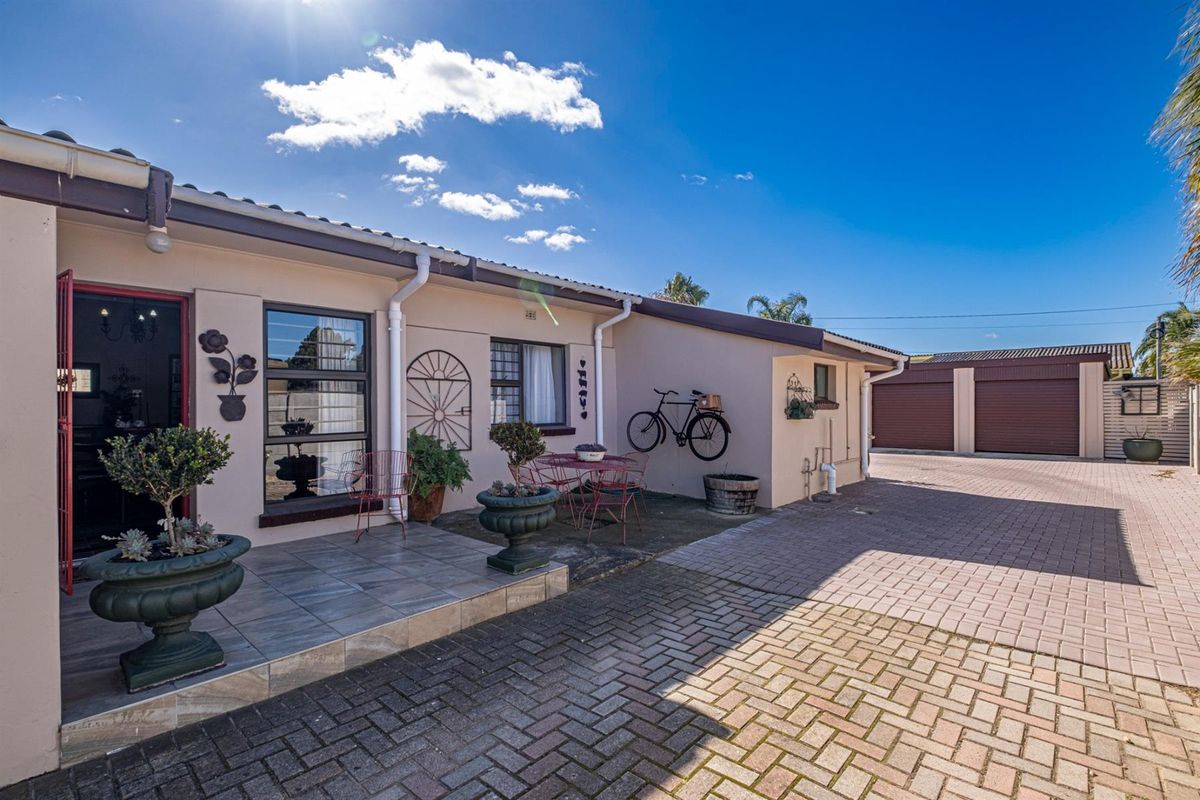 Rear exterior view featuring a paved driveway, tiled patio area, and access to a double garage with roller doors.
