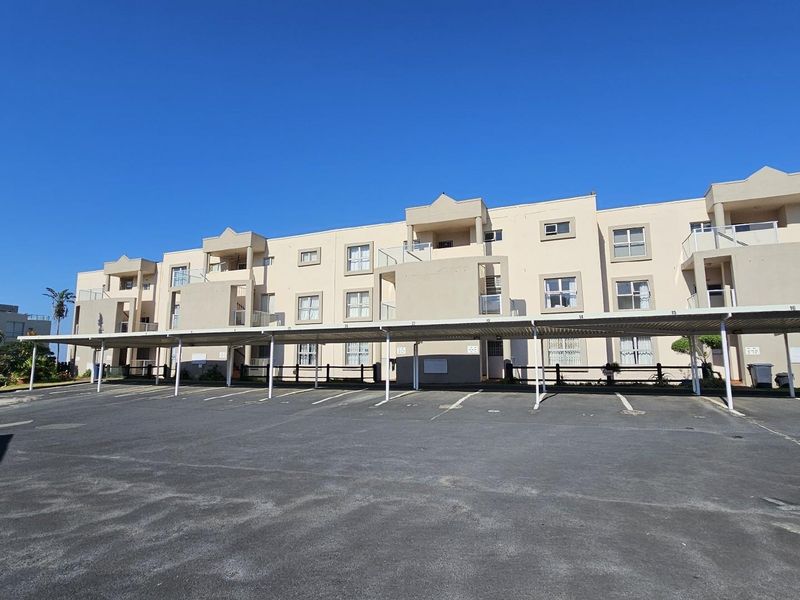Exterior view of a multi-story apartment complex featuring covered parking bays and private balconies for each unit.
