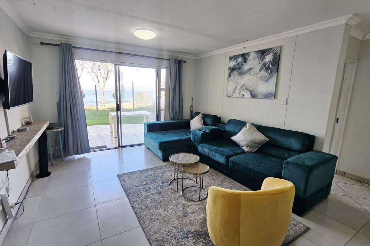 Bright living room featuring large sliding glass doors that open to a patio with scenic coastal views and tiled flooring throughout.
