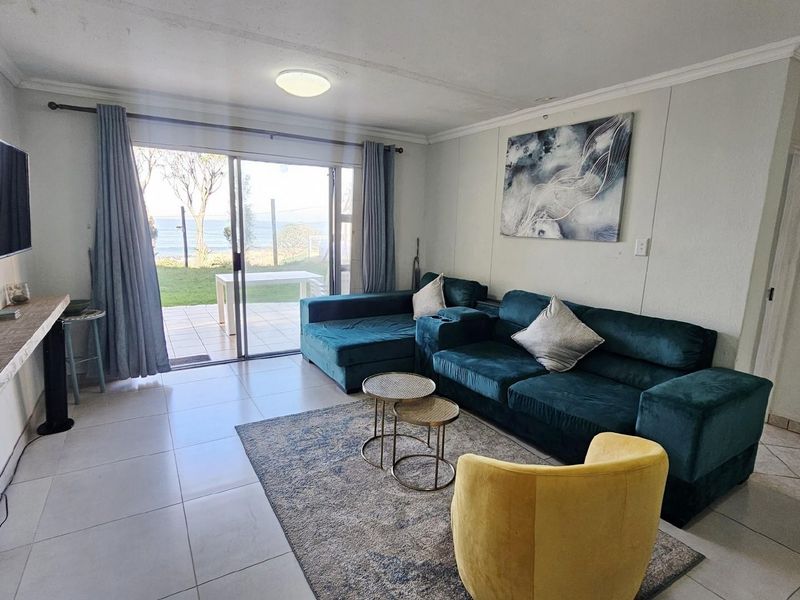 Bright living room featuring large sliding glass doors that open to a patio with scenic coastal views and tiled flooring throughout.