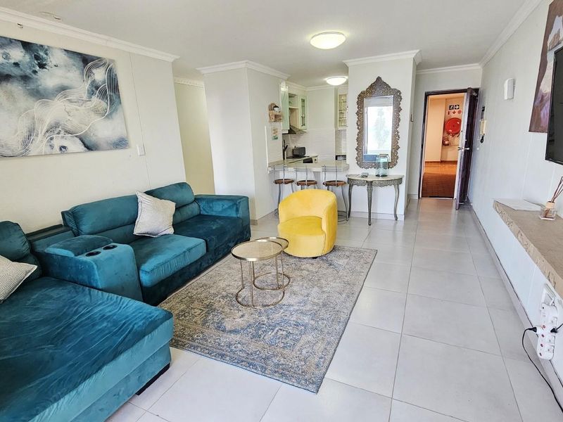 Open-plan living area featuring tiled flooring, a compact kitchen nook with breakfast bar, and direct access to the entrance hallway.