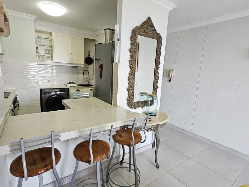 Compact open-plan kitchen featuring built-in cabinetry, stone-look breakfast counter, and tiled flooring, seamlessly integrated with the adjacent living area.