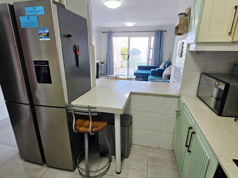 Open-plan kitchen featuring light green cabinetry, stone-look countertops, and a breakfast bar, flowing into the adjacent living area with sliding door access.