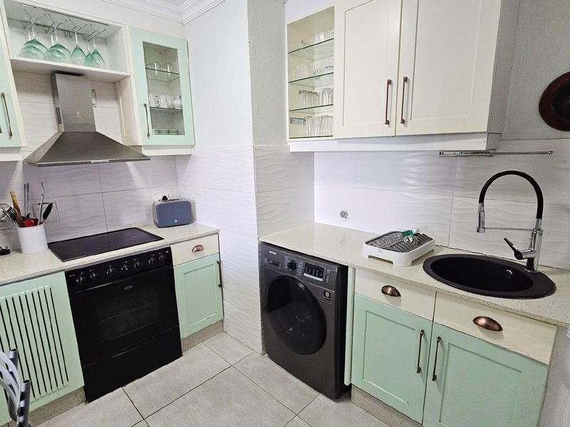 A well-maintained kitchen featuring light green and cream cabinetry, a built-in oven with extractor fan, stone countertops, and a modern black sink.