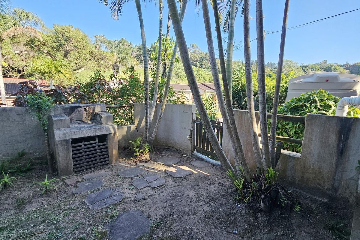 A private rear garden area featuring a built-in masonry braai, stone paving, and established palm trees enclosed by boundary walls.