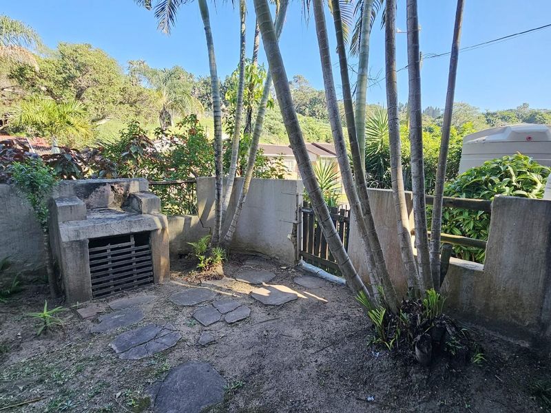 A private rear garden area featuring a built-in masonry braai, stone paving, and established palm trees enclosed by boundary walls.