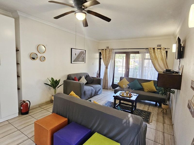 A comfortable living room featuring tiled flooring, a ceiling fan, and glass sliding doors that provide access to the outdoor area.