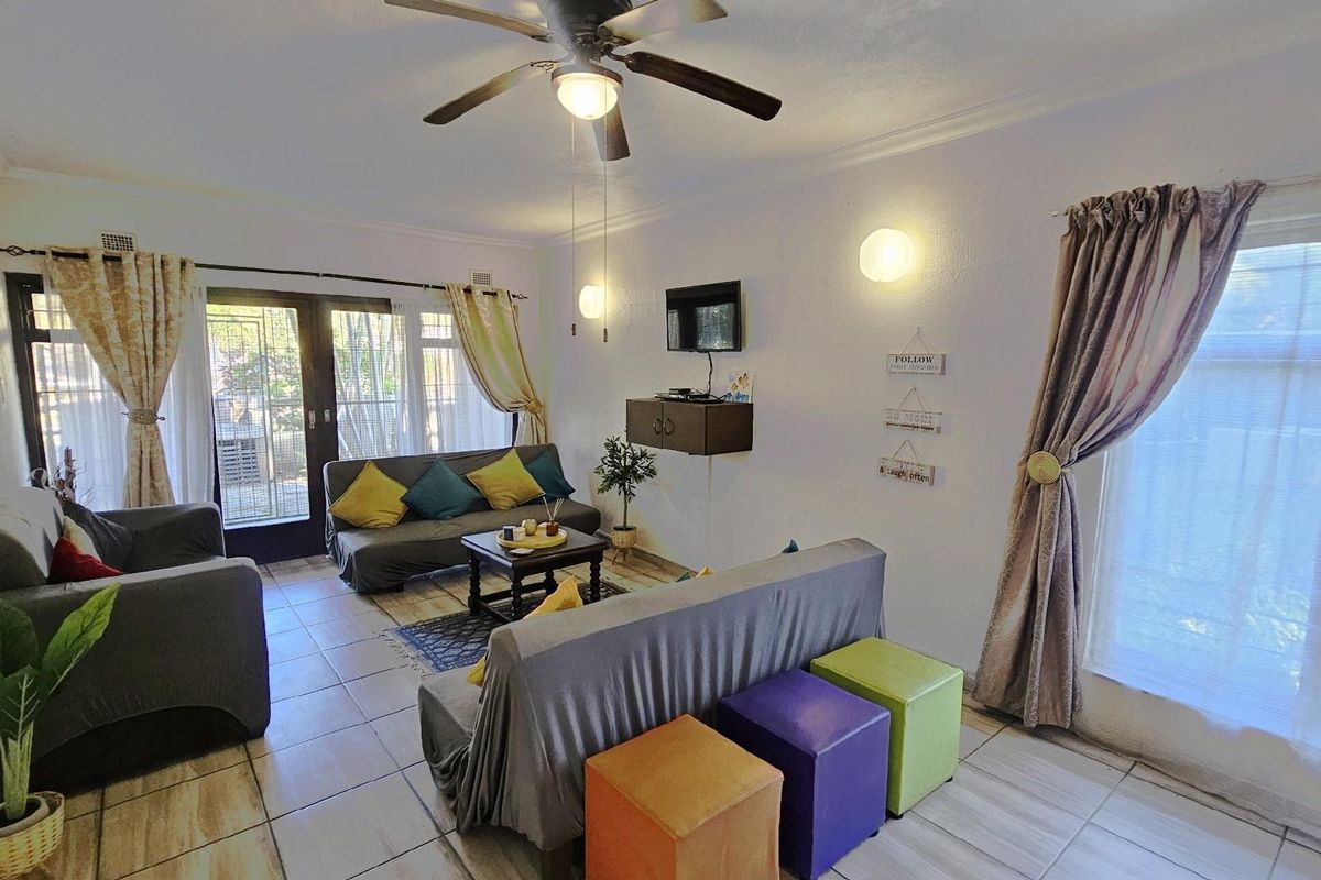 A bright living room featuring tiled flooring, a ceiling fan, and large windows providing natural light with direct access to the outdoor area.