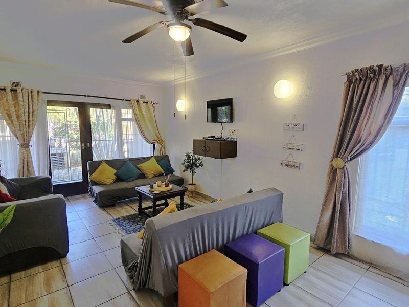A bright living room featuring tiled flooring, a ceiling fan, and large windows providing natural light with direct access to the outdoor area.