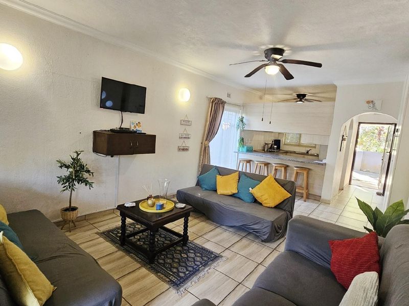 Open-plan living area featuring tiled flooring, ceiling fans, and a breakfast bar counter connecting to the kitchen space.