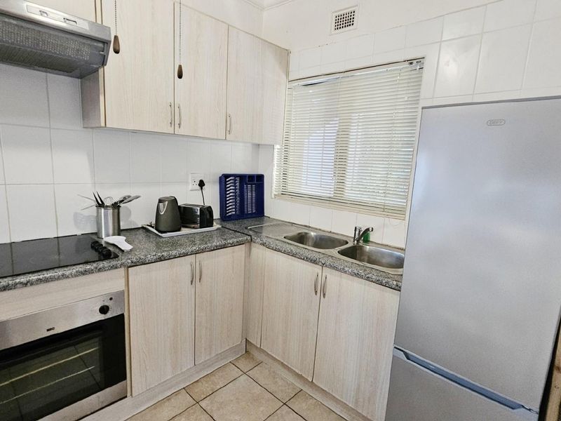 A functional kitchen featuring light wood-look cabinetry, granite-style countertops, a built-in oven, extractor fan, and a double-basin stainless steel sink.