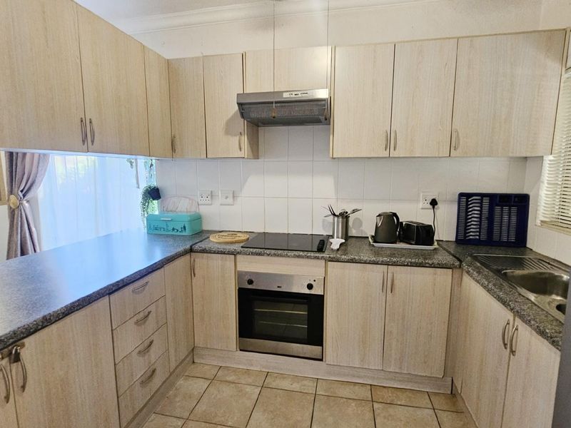 A functional kitchen featuring light wood-grain cabinetry, granite-look countertops, a built-in oven, electric hob, and stainless steel extractor fan.
