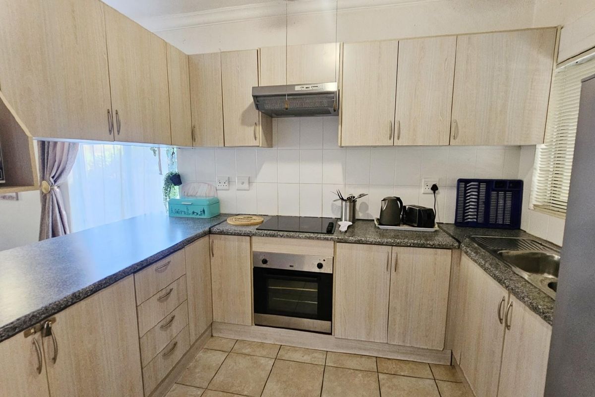 A functional kitchen featuring light wood-grain cabinetry, granite-look countertops, a built-in oven, electric hob, and stainless steel extractor fan.