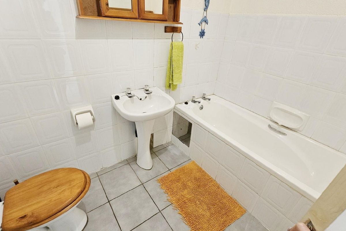 A functional bathroom featuring a white pedestal basin, a standard bathtub, and tiled walls and flooring.