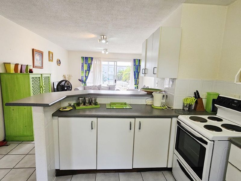 Open-plan kitchen featuring a breakfast bar, white cabinetry, and a freestanding electric stove, flowing into the adjacent living area with patio access.