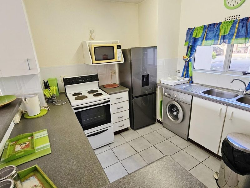 A functional kitchen featuring white cabinetry, tiled flooring, a built-in stove, and integrated space for laundry appliances.