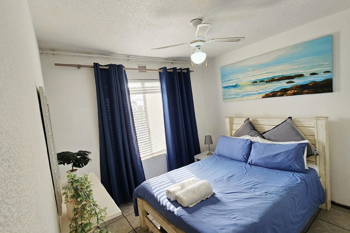 A functional bedroom featuring tiled flooring, a ceiling fan, and a window with curtain tracks, providing a comfortable and well-lit sleeping space.