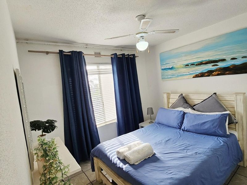 A functional bedroom featuring tiled flooring, a ceiling fan, and a window with curtain tracks, providing a comfortable and well-lit sleeping space.