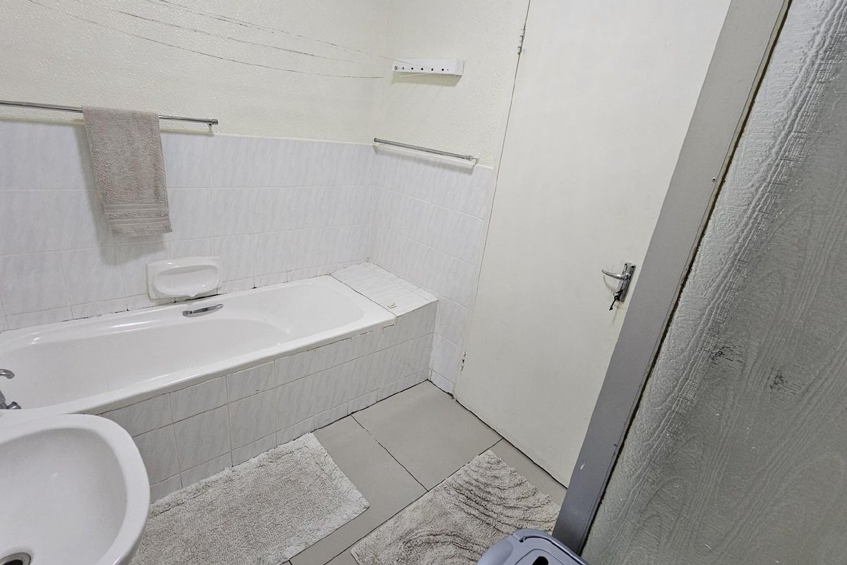 A functional bathroom featuring a built-in bathtub, tiled splashbacks, and a pedestal basin, requiring cosmetic updates to improve its overall condition.