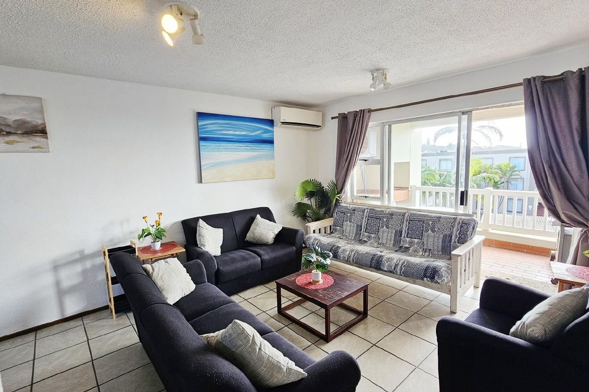 A comfortable living room featuring tiled flooring, a wall-mounted air conditioning unit, and sliding glass doors that open onto a private balcony.