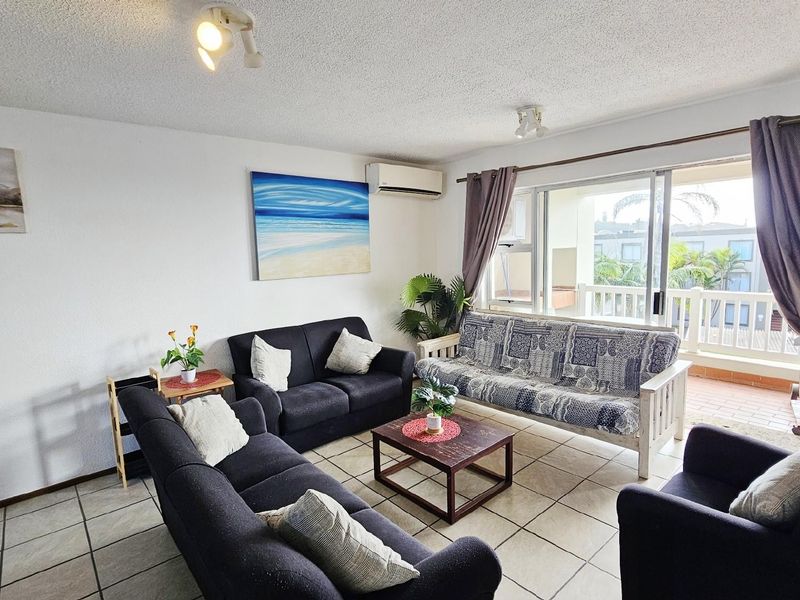 A comfortable living room featuring tiled flooring, a wall-mounted air conditioning unit, and sliding glass doors that open onto a private balcony.