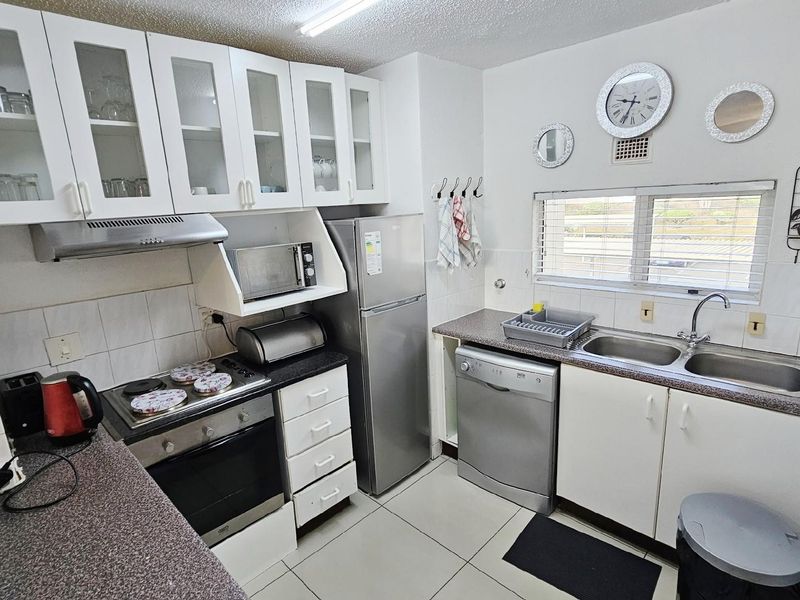 Functional kitchen featuring white cabinetry, built-in oven, hob, extractor fan, double stainless steel sink, and tiled flooring.