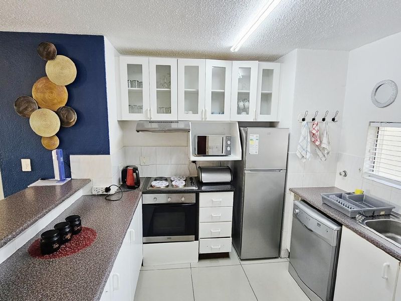 A functional kitchen featuring laminate countertops, built-in oven and hob, extractor fan, and white cabinetry with glass-fronted upper cupboards.