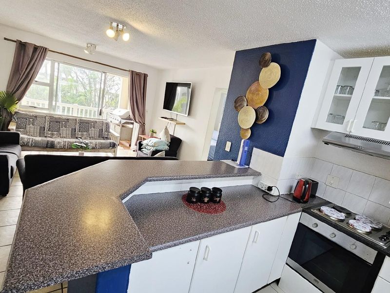 Open-plan living area featuring a kitchen with white cabinetry, a breakfast bar, and a connected lounge space with access to a balcony.