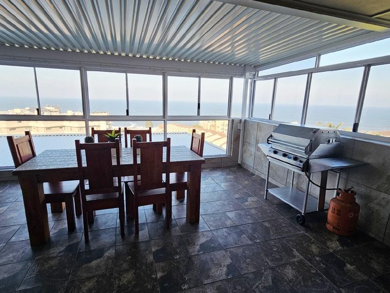 Enclosed balcony featuring tiled flooring, large windows with ocean views, and a built-in structure suitable for outdoor dining and entertaining.
