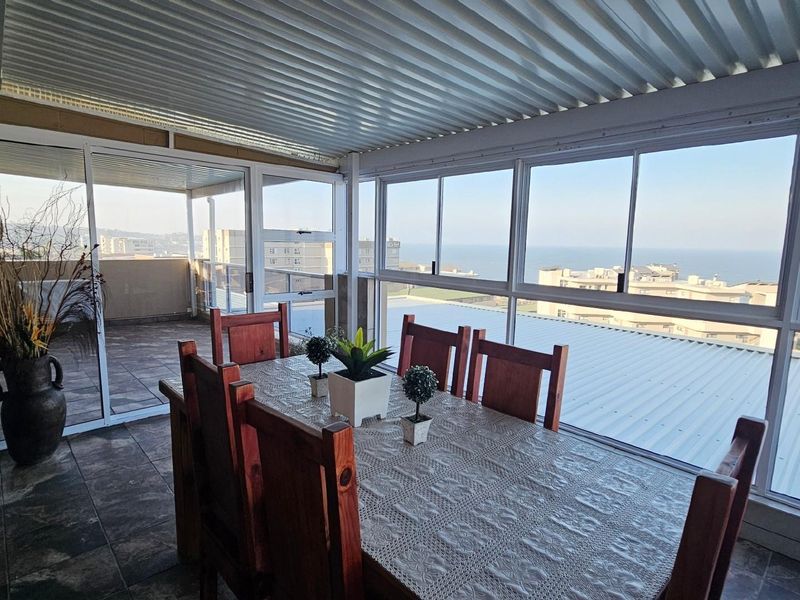 Enclosed balcony featuring tiled flooring, large sliding glass windows, and a corrugated metal roof, offering expansive coastal and urban views.