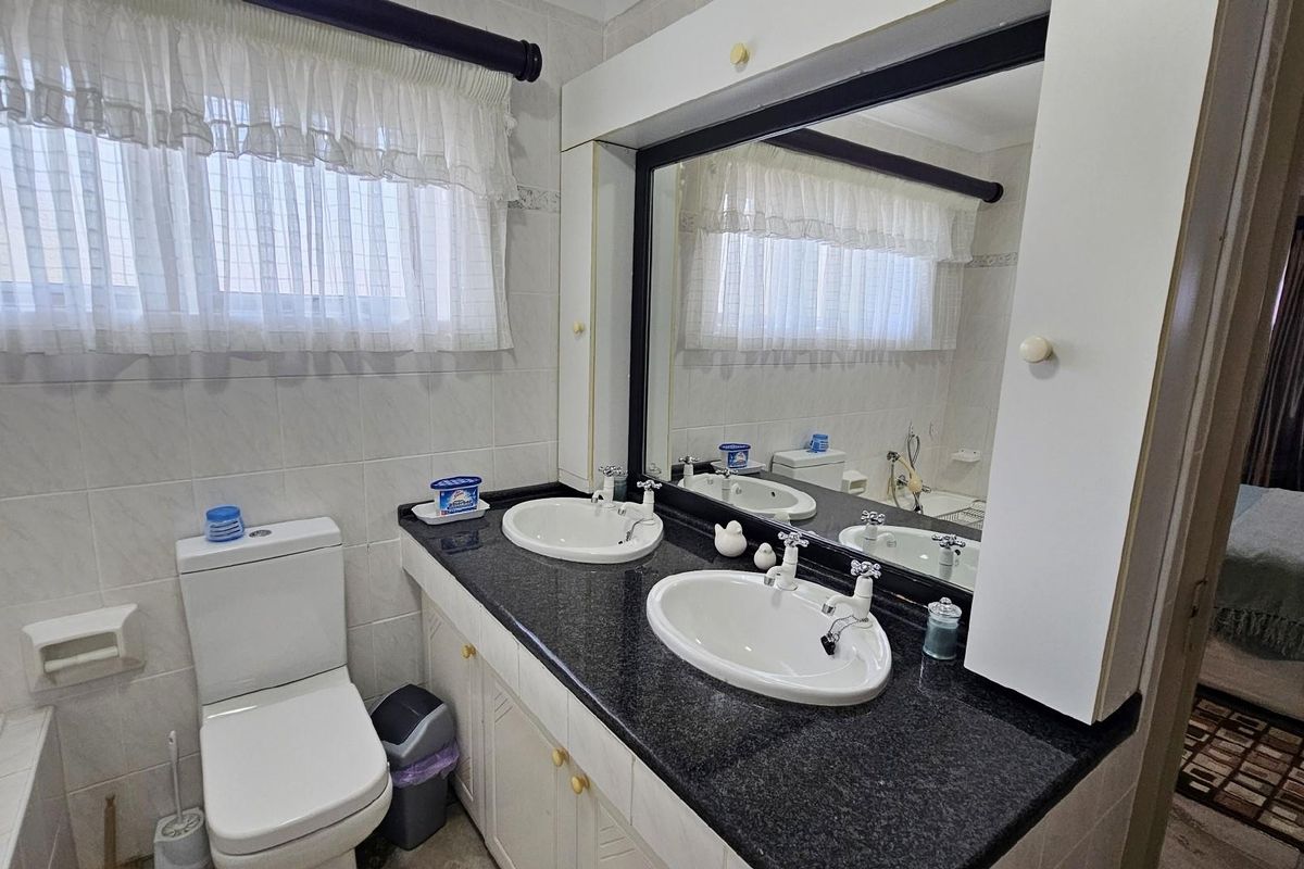 A functional bathroom featuring a double vanity with a dark granite countertop, dual basins, and a large wall-mounted mirror.