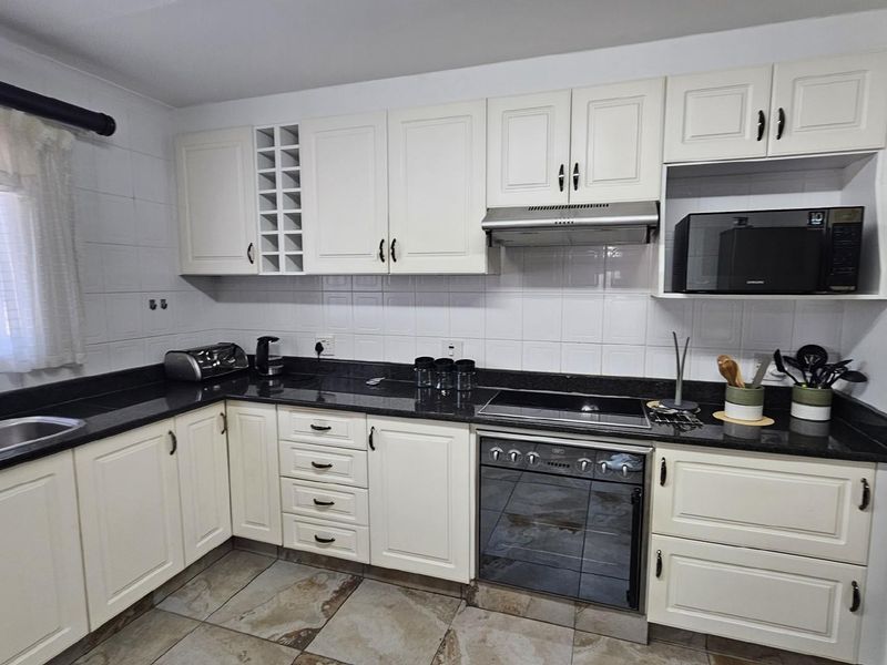 A functional kitchen featuring white cabinetry, dark granite countertops, a built-in oven with extractor fan, and tiled flooring.